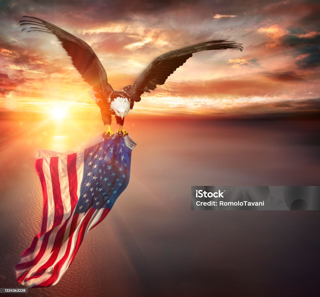Eagle With American Flag Flies In Freedom At Sunset - Vintage Toned Bald Eagle Holding Usa Flag On Ocean At Sunset - Vintage Filter American Flag Stock Photo