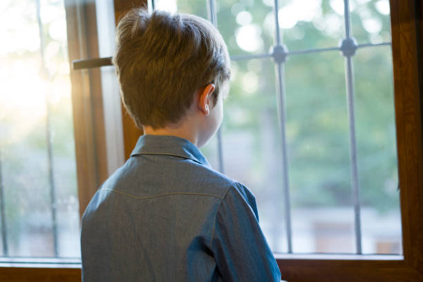 istock Young boy perching on desk and looking through the window 1324364275
