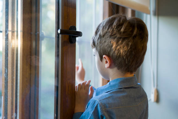 istock Young boy perching on desk and looking through the window 1324364277
