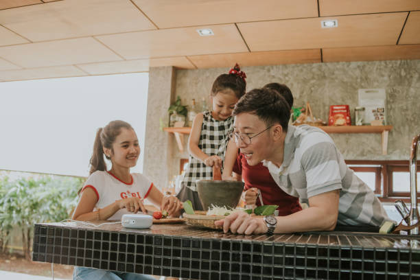 Father asking AI speaker how to cook Thai food menu from AI speaker during cooking papaya salad or Somtum in Thai kitchen - stock photo