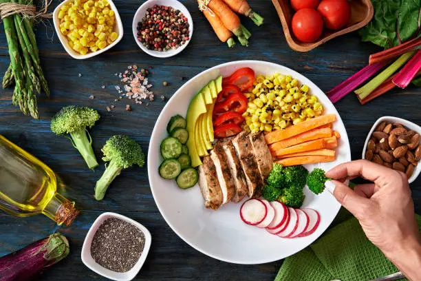 Healthy eating and diet concepts. Colorful and healthy fresh salad on rustic wood table. Included ingredients: Chicken, tomatoes, broccoli, lettuce, bell peppers, mushroom, carrots, radicchio, almonds.