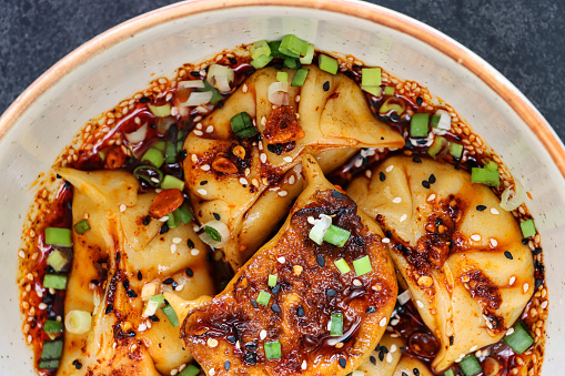 Stock photo showing an evening meal of pan fried dumplings (Momos), filled with mixed vegetables and pork drizzled with chilli oil and garnished with chopped chives and nigella seeds.