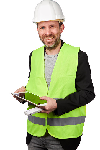 A portrait of an architect or civil engineer with a white hard hat and safety vest photographed in high resolution in the studio as a cutout against a white background. He wears casual business clothes and holds an iPad or tablet and a folding rule in his hand