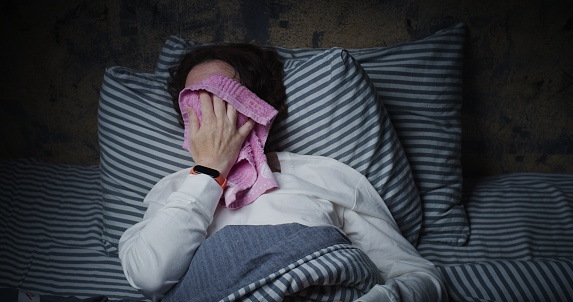 Mature woman is trying to sleep in bed but suffering from heat
