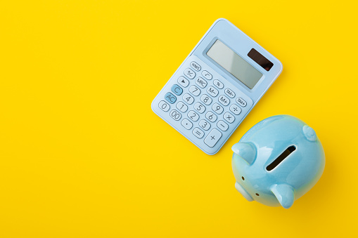 Piggy bank with calculator on yellow background, top view
