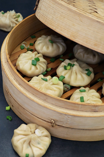 Stock photo showing an evening meal of steamed dumplings (Momos), filled with mixed vegetables garnished with chopped spring onion and nigella seeds in bamboo steamer.