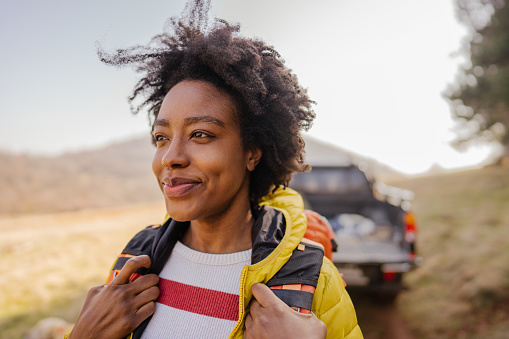 Photo of a young smiling woman carrying a backpack during the road trip