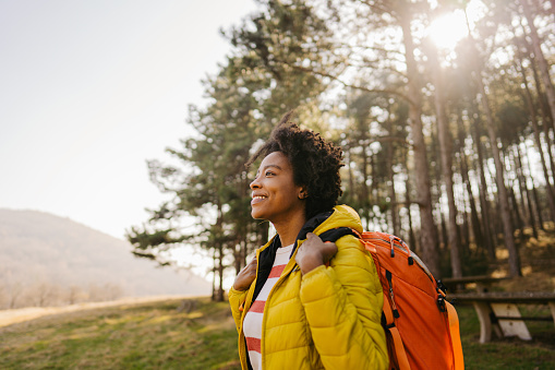 Photo of a young smiling woman carrying a backpack and hiking in the nature