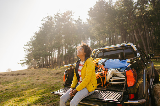 Photo of a young smiling woman enjoying nature while sitting on a pick-up truck