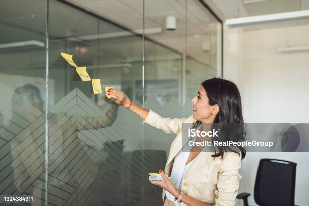Happy Smile Mid Adult Business Woman Write A Message And Stick On A Glass Board Stock Photo - Download Image Now