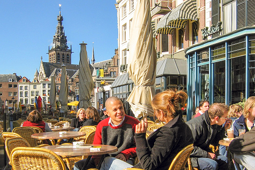 A young couple sits on a terrace at the Grote Markt in Nijmegen, the Netherlands. In the background the historic buildings of the Grote Markt, including the St Stevenstoren.