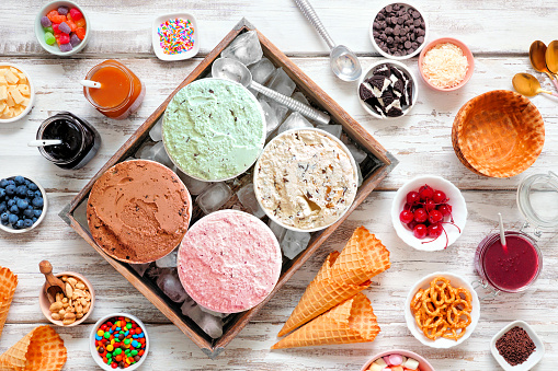 Mesa buffet de helados de verano con una variedad de sabores y coberturas dulces. Vista cenital sobre madera blanca rústica. photo