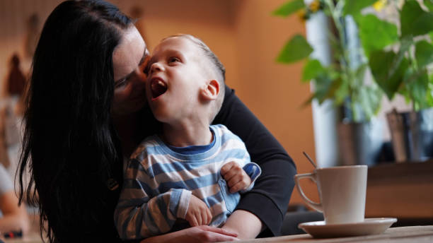 close up portrait of a little boy with special needs and mom laughing at a table in a cafe, lifestyle. mom's love for her child, inclusion.happy disability kid concept - neurology child stockfoto's en -beelden