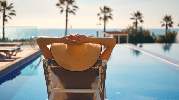 Rear view woman wear straw hat lying on deckchair on poolside