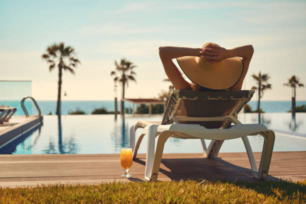 vue arrière femme porter chapeau de paille se disant sur transat sur le bord de la piscine - rebord de piscine photos et images de collection