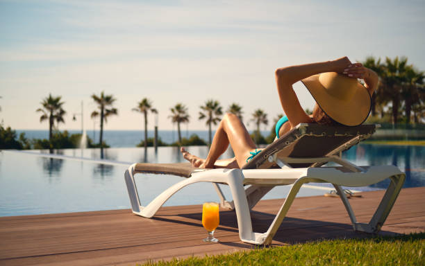 istock Rear view woman wear straw hat lying on deckchair on poolside 1324410549
