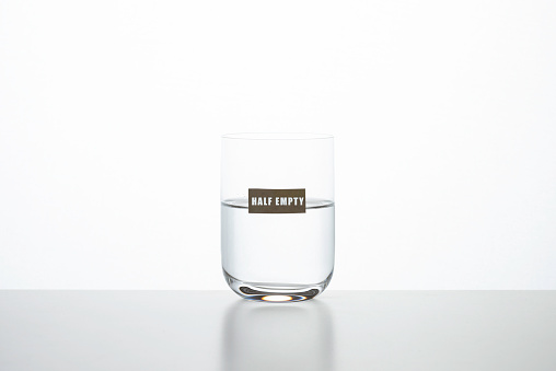 Drinking glass with water on white background. Half empty is written on  glass. Representing point of view about facts.