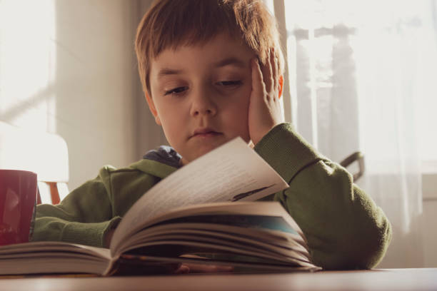 istock Cute boy reading a book at home 1324444797