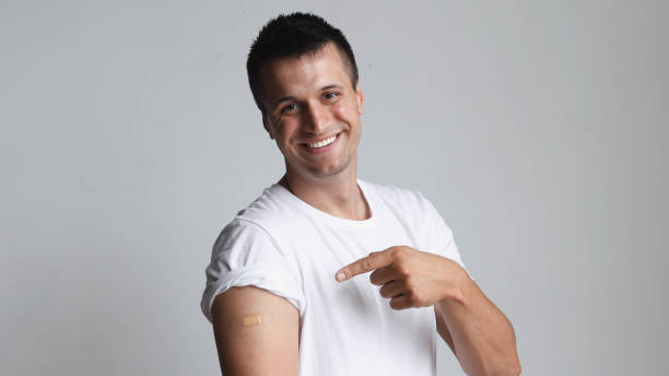 istock Covid-19 vaccinated caucasian smiling man showing arm with plaster, gray background 1324459125
