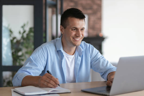 istock Friendly satisfied caucasian man student, taking notes in notebook during lecture sitting at table in home, online studying at home concept distance education, video call, smiling 1324459896