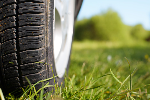 Nature trip concept. Close-up of a car wheel outdoors. Car standing on the grass on a sunny summer day, selective focus.