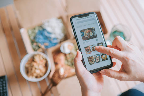 hochwinkelansicht nahaufnahme asiatische frau mit essen lieferservice bestellen lebensmittel online mit mobilen app auf smartphone im wohnzimmer in einem gemütlichen haus - lebensmittel stock-fotos und bilder