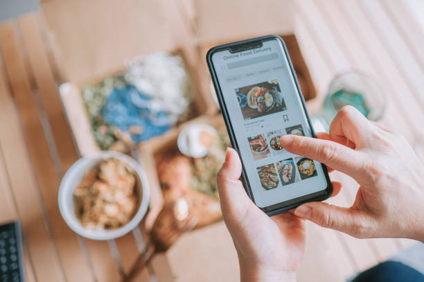 vue à angle élevé une femme asiatique utilisant un service de livraison de repas commande de nourriture en ligne avec une application mobile sur smartphone dans le salon d’une maison confortable - food photos et images de collection