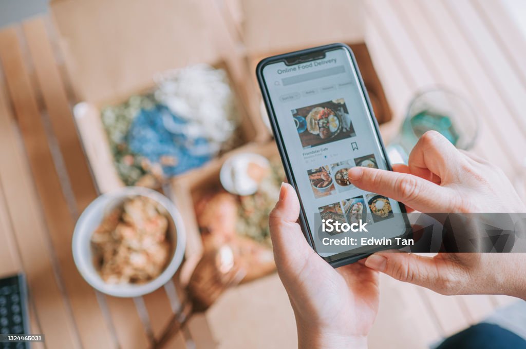 high angle view Close up Asian woman using meal delivery service ordering food online with mobile app on smartphone in the living room at a cozy home Delivering Stock Photo