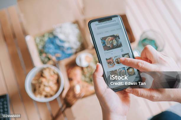 High Angle View Close Up Asian Woman Using Meal Delivery Service Ordering Food Online With Mobile App On Smartphone In The Living Room At A Cozy Home Stock Photo - Download Image Now
