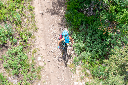 June 19, 2021 - Park City, Utah, USA: A woman mountain biker is riding down a mountain trail in Park City, Utah.  This shot was taken on a hot summer weekend from a ski lift that passed over the top of the trail.