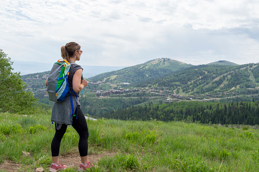 This shot was taken from the top of one of the mountains surrounding Park City, Utah.  In the distance are more of the mountains and the ski areas surrounding the city.  This woman hiker carrying a backpack is admiring the view after riding to the top of the mountain on a ski lift.