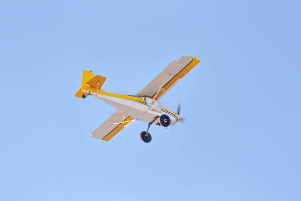 A small white and yellow plane flies in the blue sky