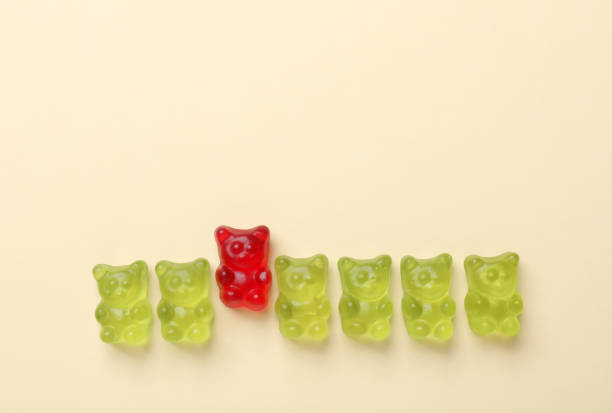 istock Red jelly bear among green ones on beige background, flat lay. Uniqueness concept 1324478823