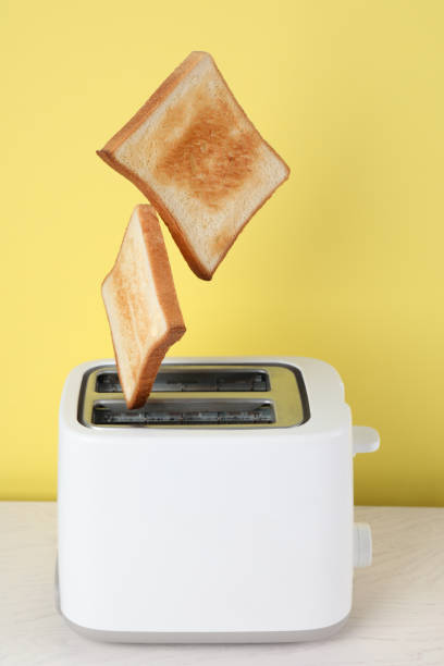istock Bread slices popping up from modern toaster on white wooden table 1324478891