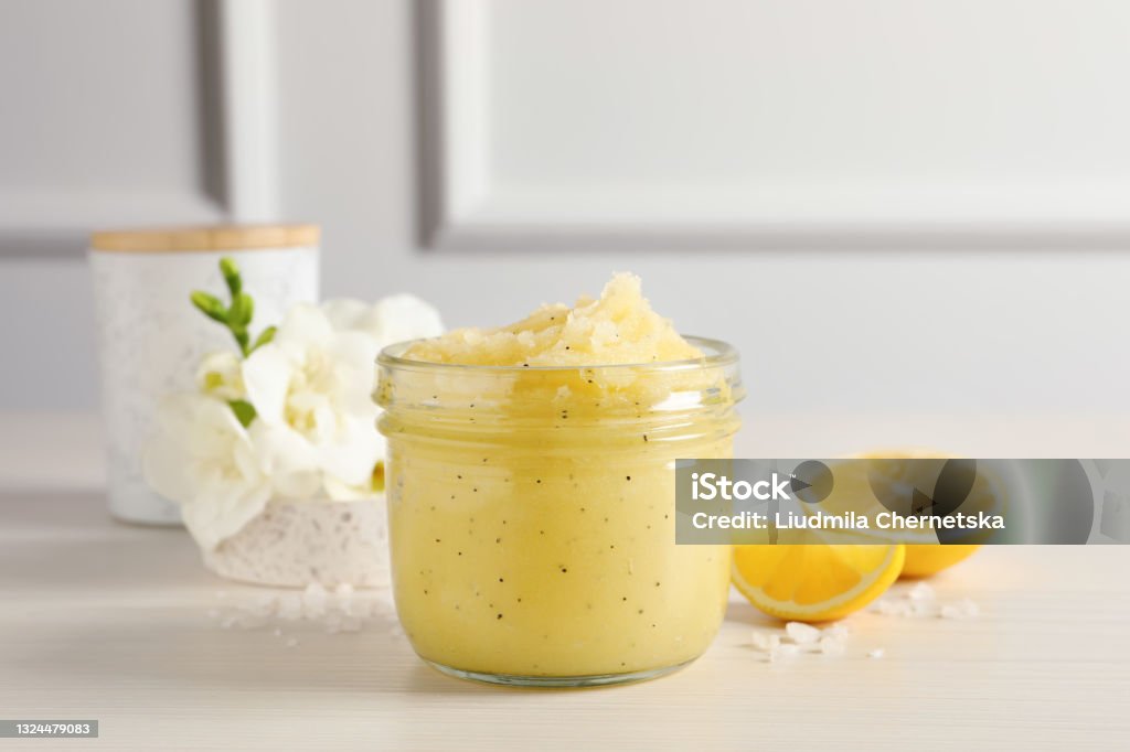 Body scrub in glass jar, freesia flowers and lemon on wooden table Exfoliation Stock Photo