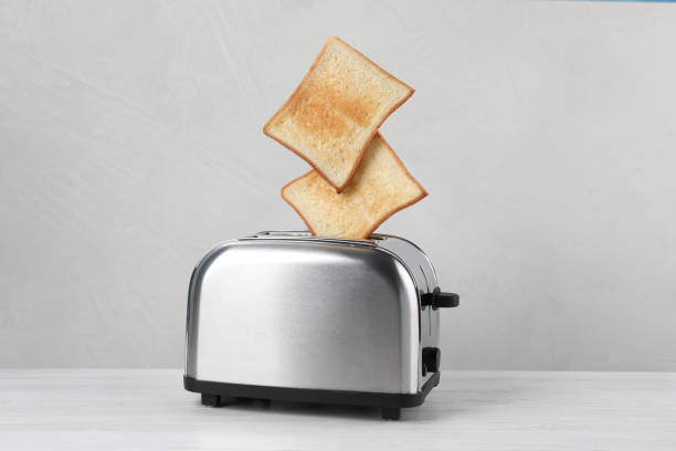 bread slices popping up from modern toaster on white wooden table - toaster imagens e fotografias de stock