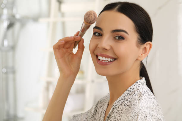 hermosa joven aplicando polvo facial con cepillo en el baño de casa - powder make up fotografías e imágenes de stock