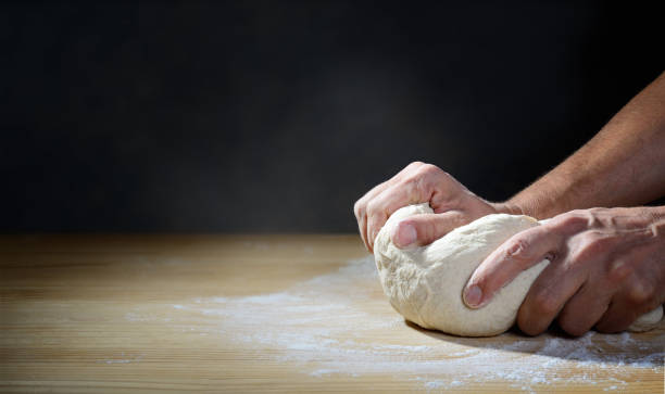 istock Hands kneading dough for bread or pizza on wooden pastry board. Dark backdrop, space for text. 1324496967