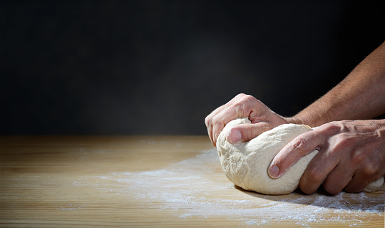 Close-up of the baker hands, dough with soft wheat flour, copy space.