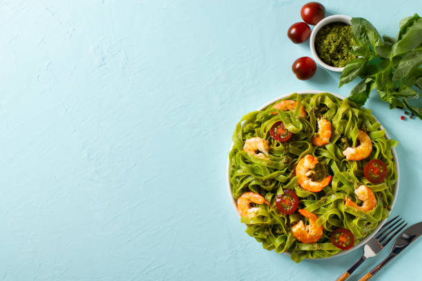 istock Green pasta with shrimp, basil and tomato on blue background, top view, copy space, flat lay 1324501799