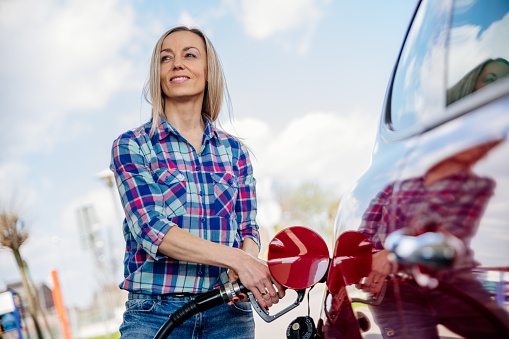 Smiling woman refueling the gas tank at fuel pump