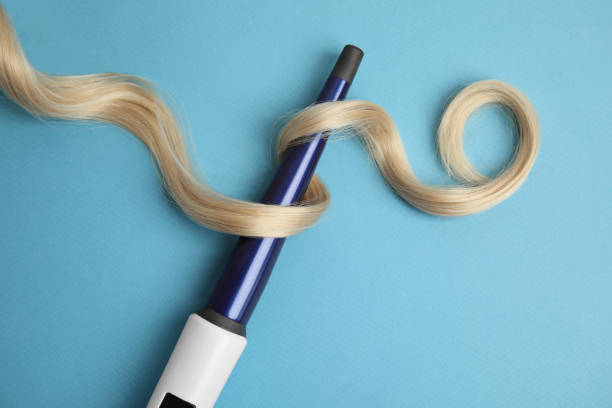 Curling iron with blonde hair lock on light blue background, flat lay Curling iron with blonde hair lock on light blue background, flat lay iron appliance photos stock pictures, royalty-free photos & images