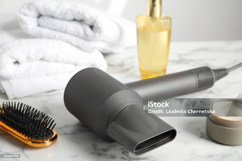 Hair care products, dryer and brush on white marble table Hair Dryer Stock Photo