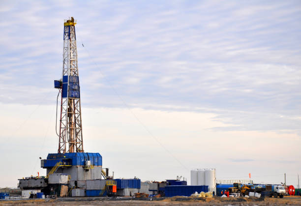 Fracking drilling rig and oil field infrastructure operating during sunset on open plains. Active oil and gas extraction site with drilling tower, storage tanks, and support facilities highlights shale drilling, fossil fuel production, and large-scale fuel and power generation in a rural landscape.