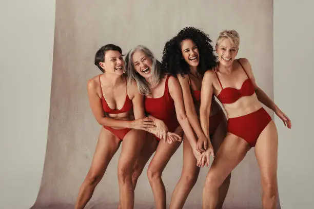 Women of all ages having fun in their natural and aging bodies. Four happy and body positive women celebrating their bodies while wearing red swimwear in studio.