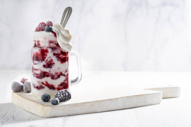 batido de yogur de frambuesas desbordamiento con bayas congeladas - yogurt yogurt container strawberry spoon fotografías e imágenes de stock