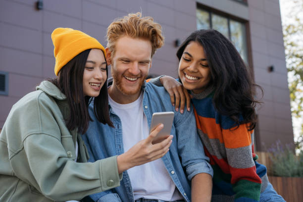 istock Multiethnic people using mobile phone watching videos outdoors. Group of smiling hipster friends shopping online. Students studying together, distance learning 1324510823