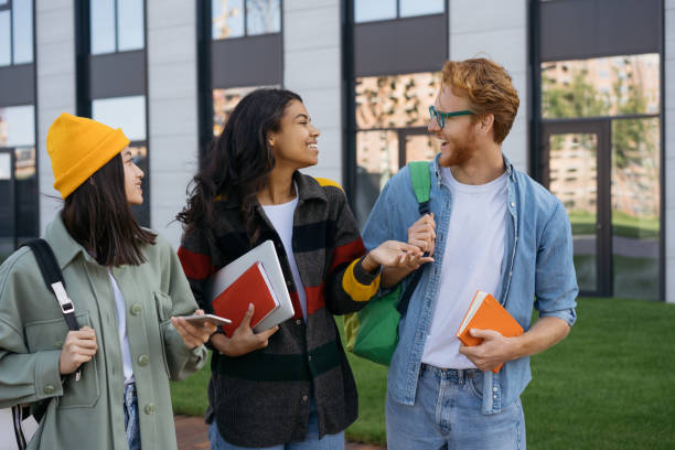 istock Multiracial smiling students with books and backpacks walking on university campus, talking. Emotional friends wearing casual clothing communication together outdoors. Education concept 1324510933