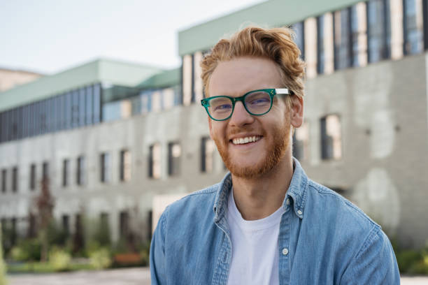 erfolgreicher student mit blick auf kamera stehen in universitätscampus, bildungskonzept. porträt eines hübschen irischen mannes trägt stilvolle brille posiert für bilder - irish culture stock-fotos und bilder