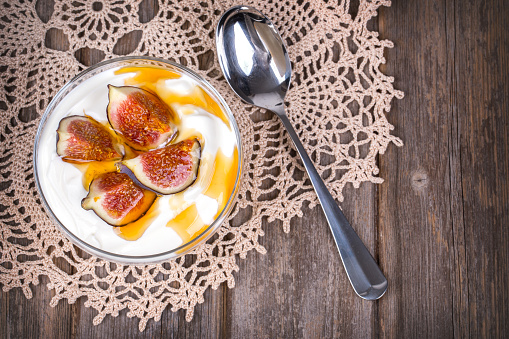 Greek yogurt with figs and honey, in a glass bowl over old lace tablecloth.